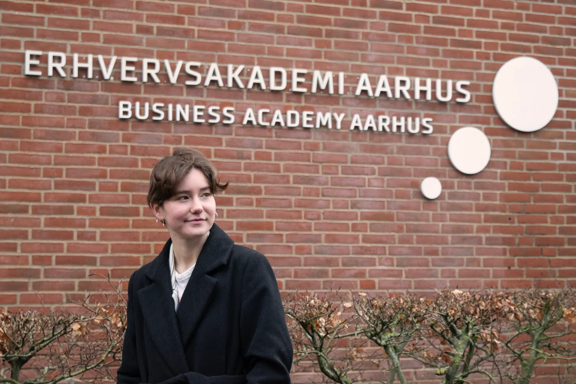 Girl standing in front of Erhvervsakademi Aarhus sign