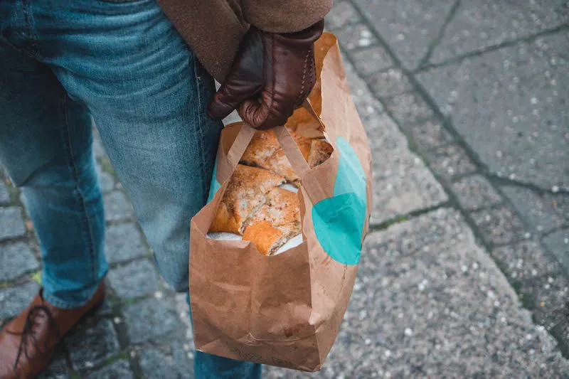 Man holding a Too Good To Go paper bag with lots of bread inside.