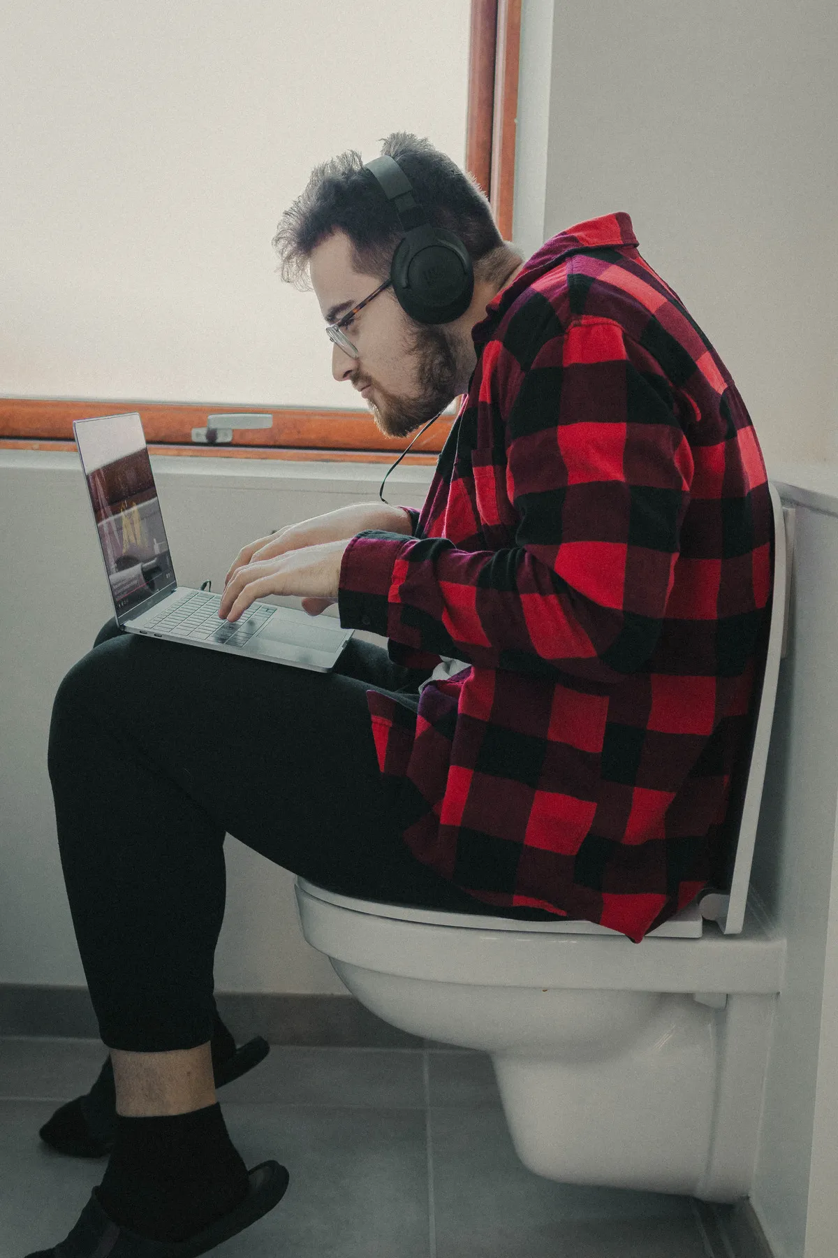 Student watching online lectures on his laptop, while sitting on the toilet (dressed)